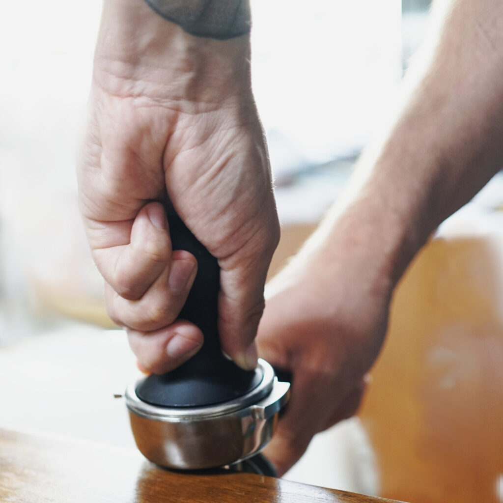 zwei Händen verdichten Espresso in einem Siebträger